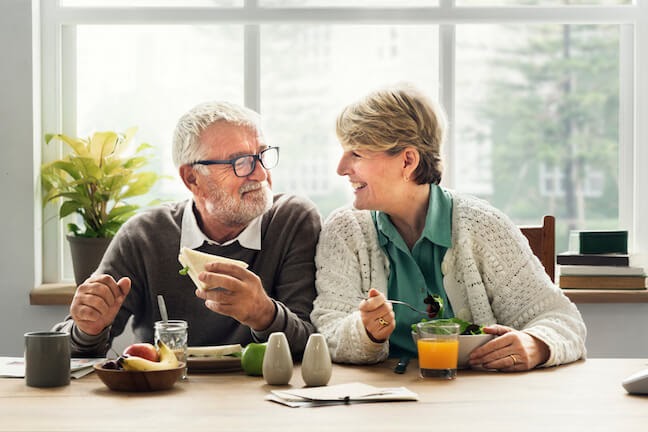 elderly couple enjoying breakfast, orange juice, glasses, white sweater, gray sweater
