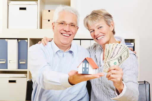 elderly couple holding home replica, cash, blue button up shirt